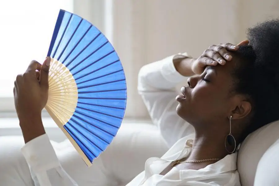 Woman using a fan while awaiting AC replacement
