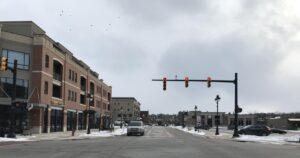 Brick buildings line a wide small-town street. Light snow blankets the ground. A red traffic light hangs overhead in cloudy weather.