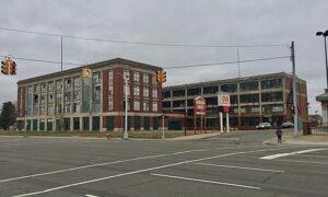 A large, multi-story industrial building rises at a street corner as traffic lights and a CVS Pharmacy sign mark the cloudy foreground.