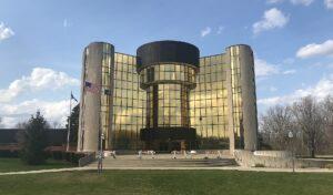 Mirrored gold glass covers the modern building’s facade, with two columns, US and state flags, and barriers in front.