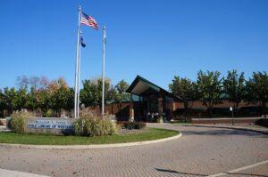 A modern brick library building sits in sunlight, with three flagpoles and a "Public Library of Westland" sign out front.