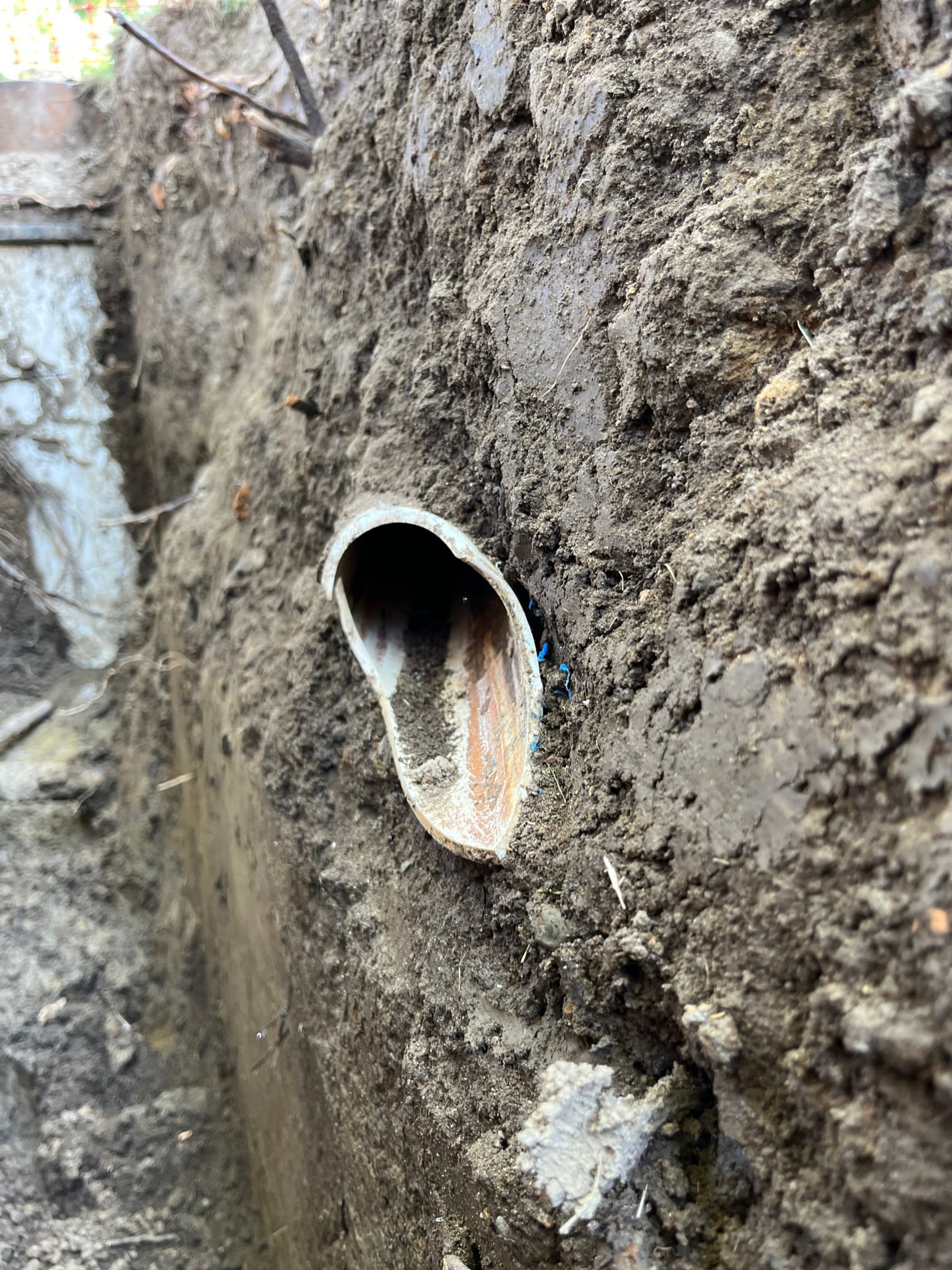 A damaged, partially exposed metal pipe juts from a dirt and concrete wall at a construction site. Fixing it now prevents costly repairs.